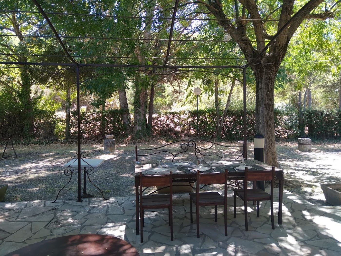 Grande table en bois et chaises sous la treille, lumière filtrée par les arbres