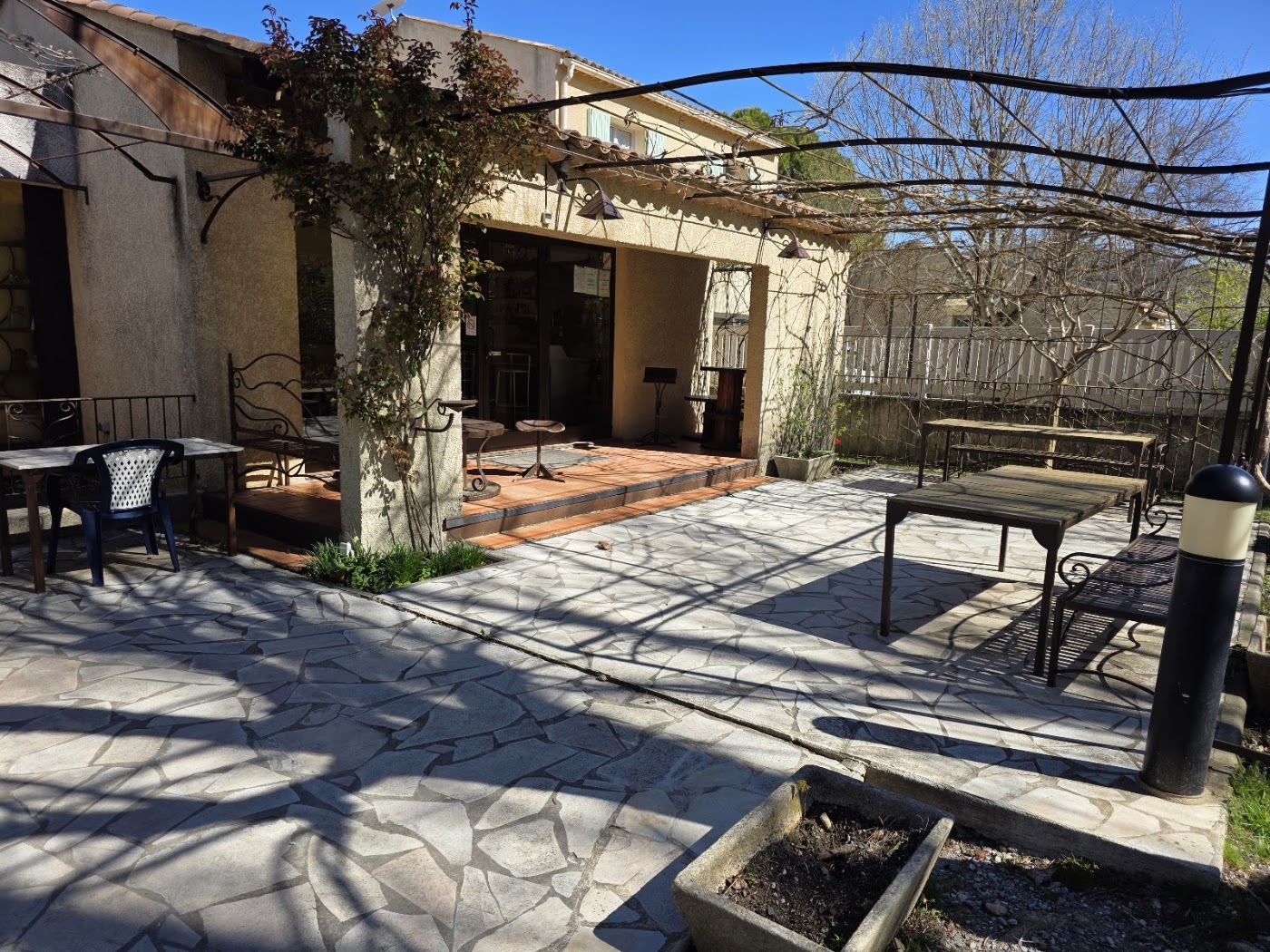 Cour dallée de pierre sous une pergola, avec tables et chaises