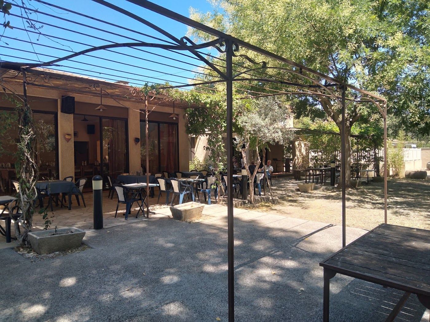 Terrasse ombragée avec pergola métallique, tables dressées et parking